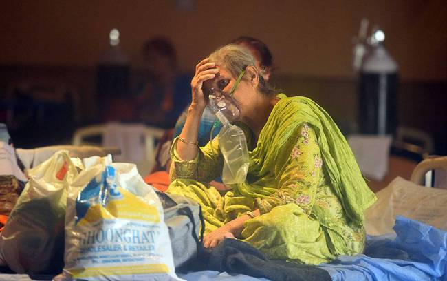 印度新德里，一名妇女坐在医院临时的新冠肺炎护理中心内的病床上吸氧